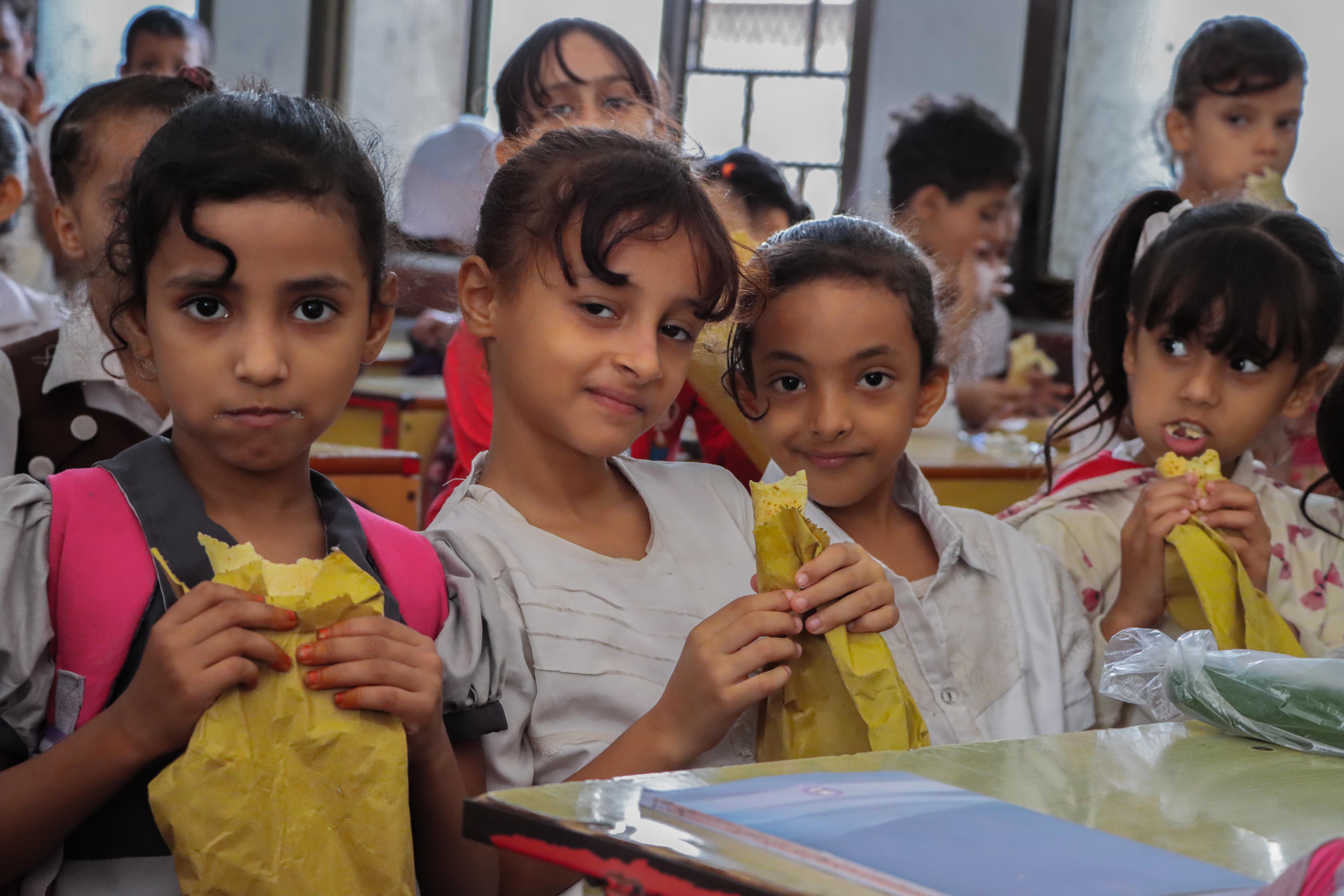 Schulkinder aus Madagaskar sitzen auf Bänken in einem kleinen Klassenraum mit gefüllten Tellern in der Hand